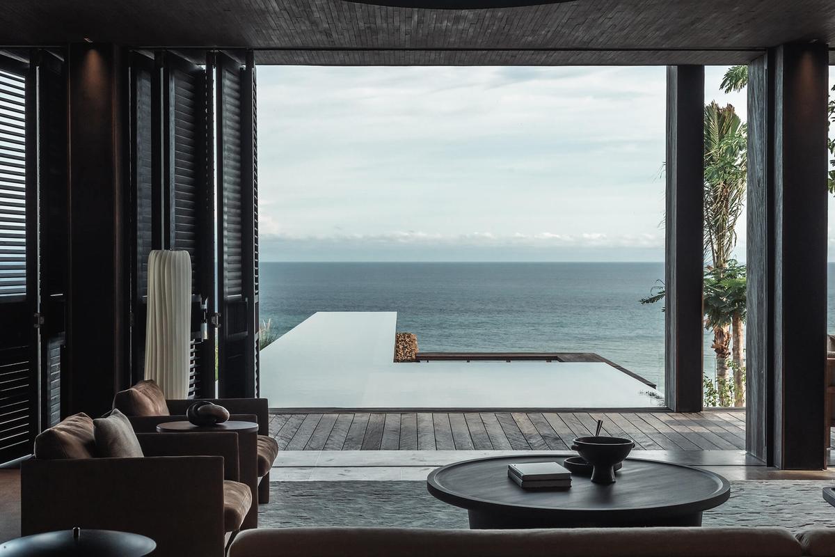 A shaded living room opening onto a dark pool and the ocean horizon